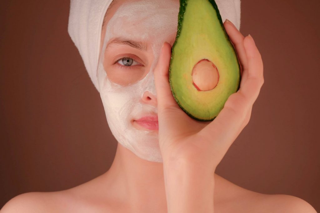 Nos conseils pour utiliser l'huile d'avocat naturelle Avodé. Jeune femme qui porte un masque de beauté à l'avocat et un avocat devant l’œil, pour améliorer la santé