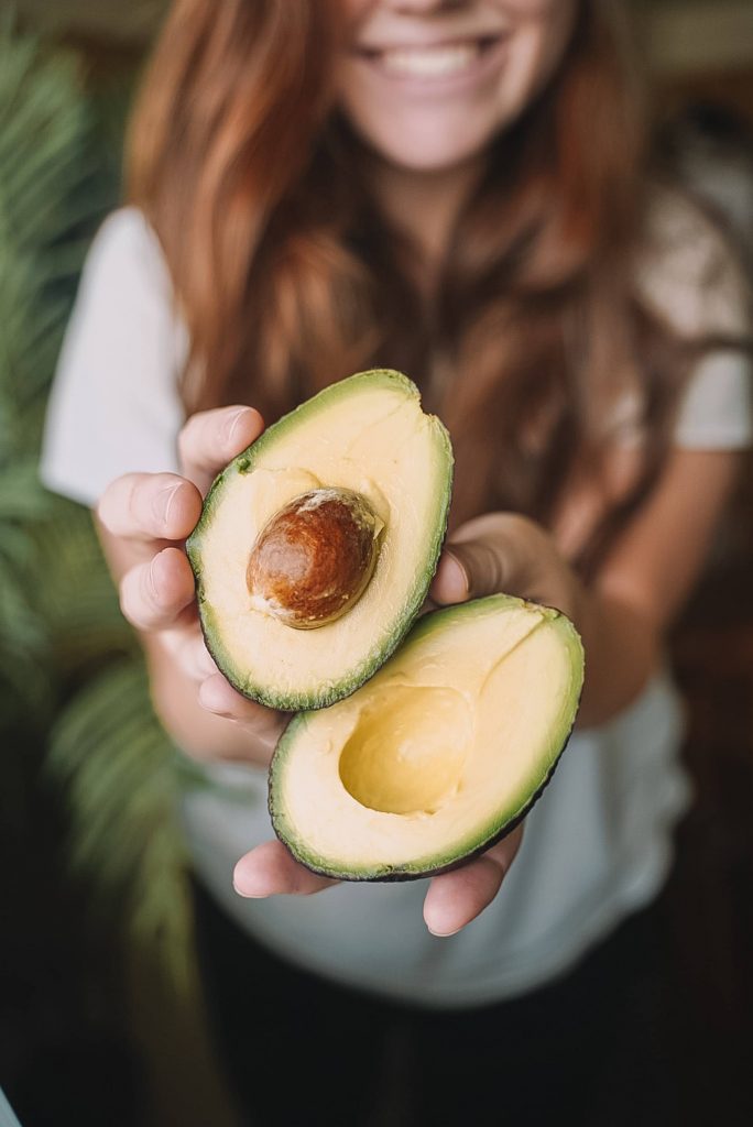 Jeune femme souriante présentant un avocat superaliment coupé en deux.