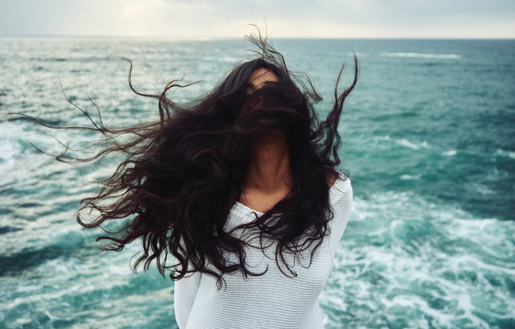 La beauté des cheveux est magnifiée par l'huile d'avocat naturelle Avodé. Femme avec les cheveux emmêlés par le vent devant la mer. comment utiliser l'huile d'avocat naturelle Avodé.